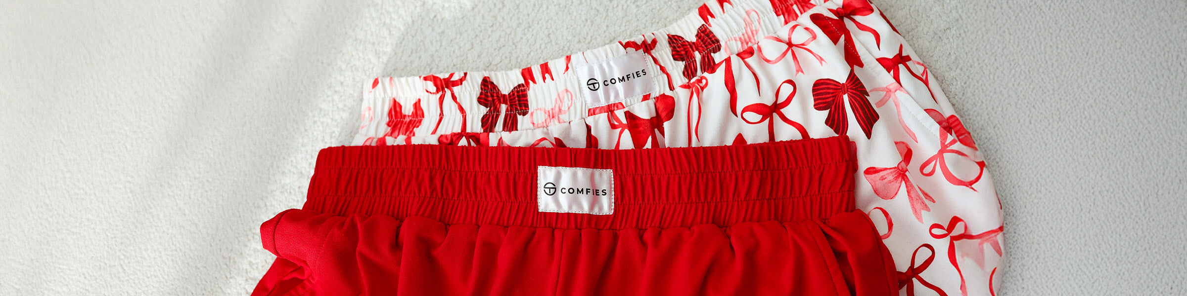 Close-up of red pajama shorts layered over red-and-white bow-pattern pajama pants, showing elastic waistbands and Comfies labels