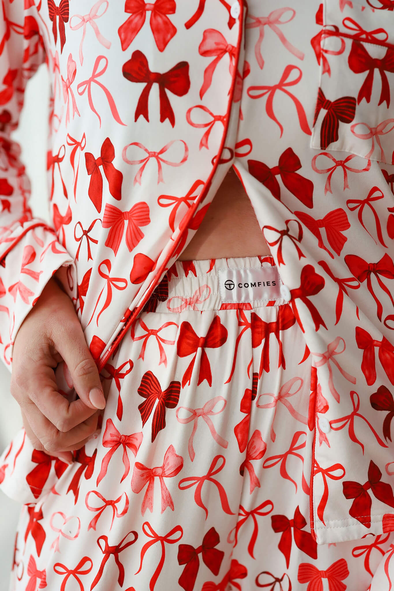 Close-up of long sleeve pajama pants with elastic waistband and red bow pattern on white fabric, showing soft, lightweight material and relaxed fit.