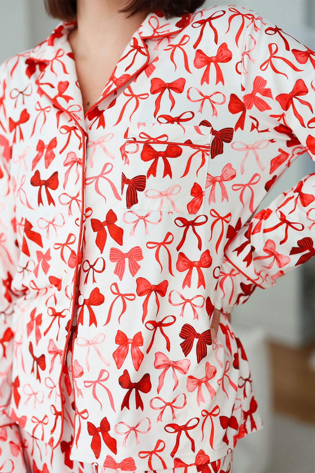 Close-up of long sleeve pajama top with button front, collar, and chest pocket, featuring an all-over red bow print on white fabric.