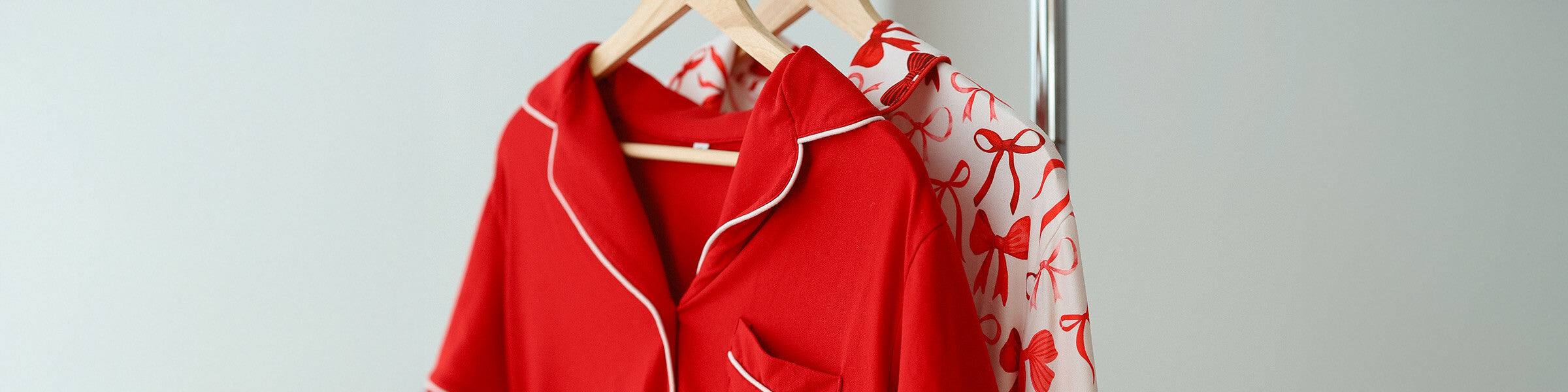Red and white pajama tops hanging on wooden hangers, featuring cozy fabric, contrast piping, and a bow pattern