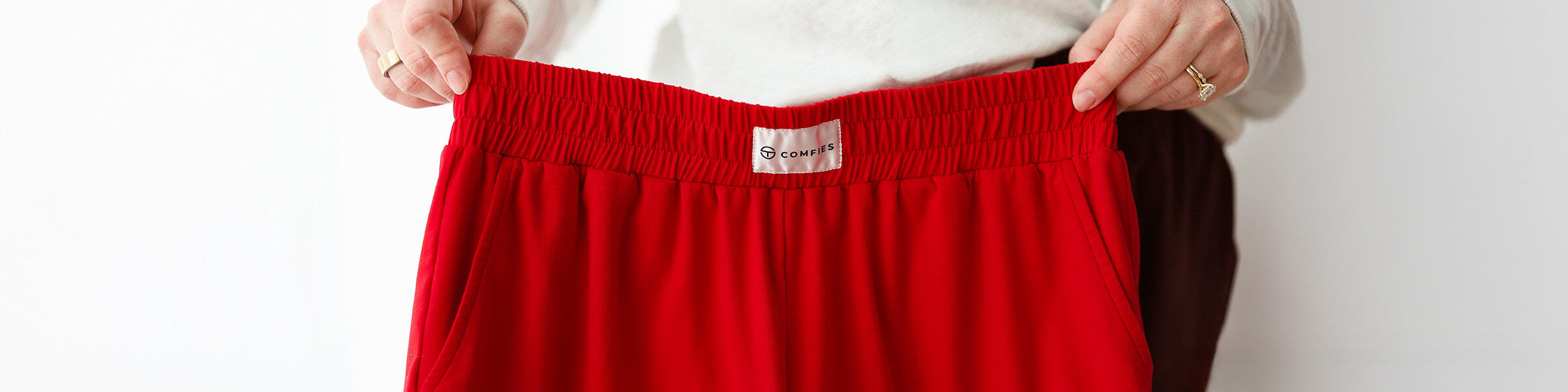 Hands holding red pajama pants with elastic waistband and Comfies label